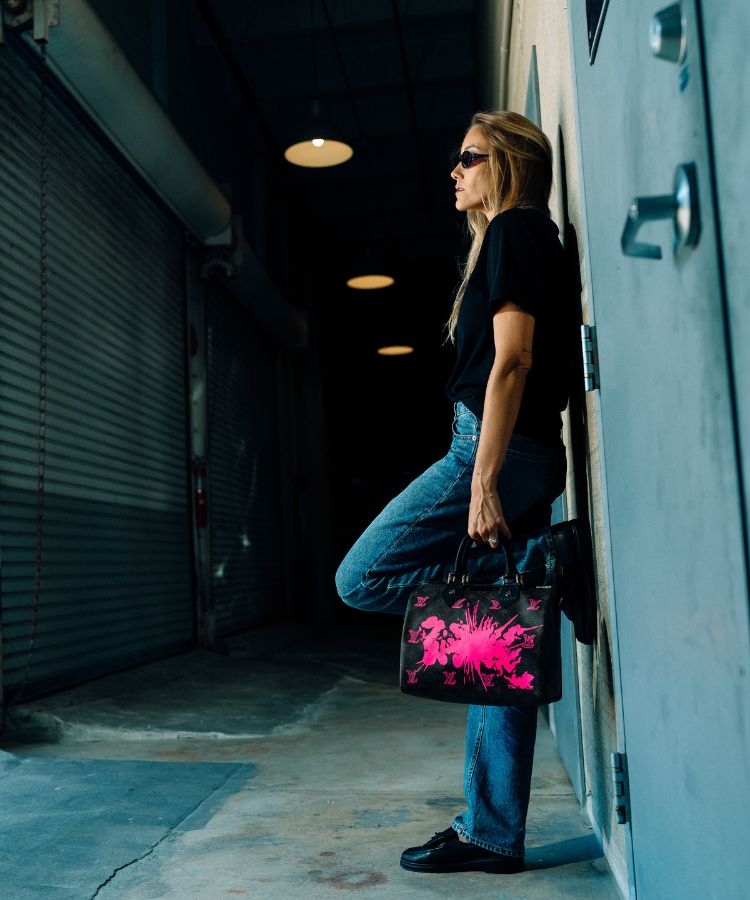 Person holding a black bag with pink design in a dimly lit alleyway
