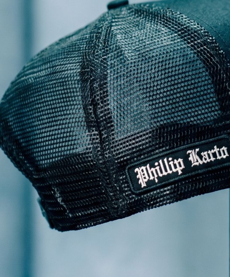 Black mesh cap with 'Phillip Karto' embroidered logo on a blurred background