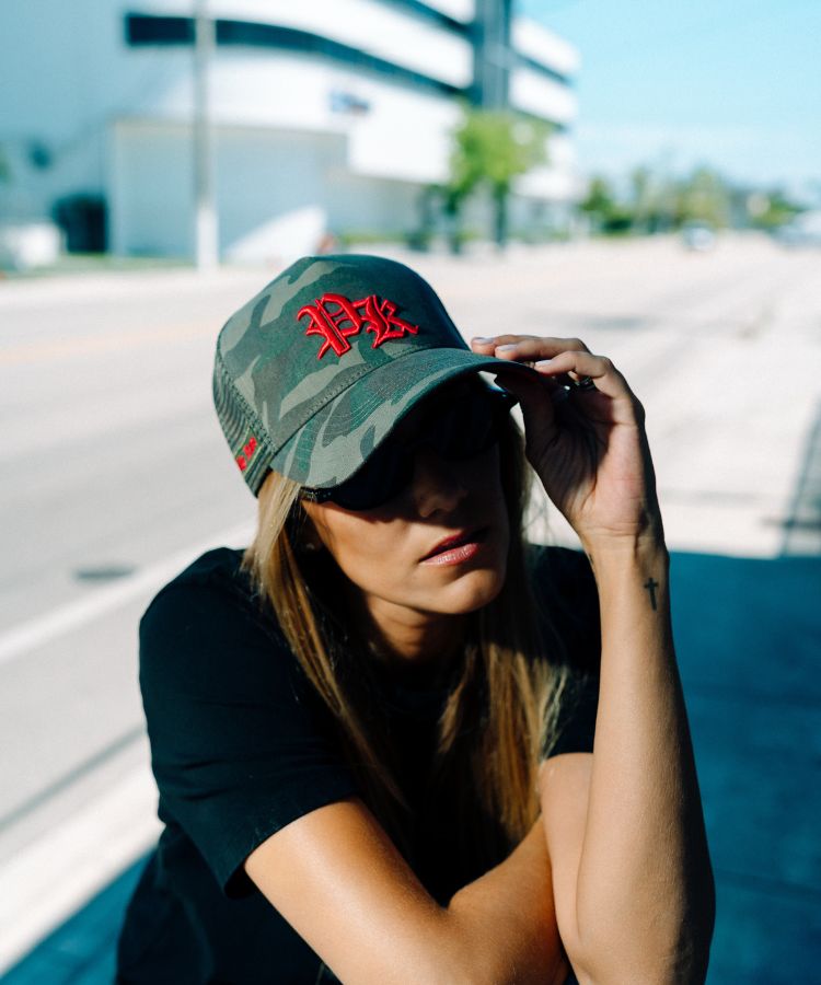 Person wearing a green camouflage cap with red logo outdoors. It's a Philip Karto Camouflage PK cap