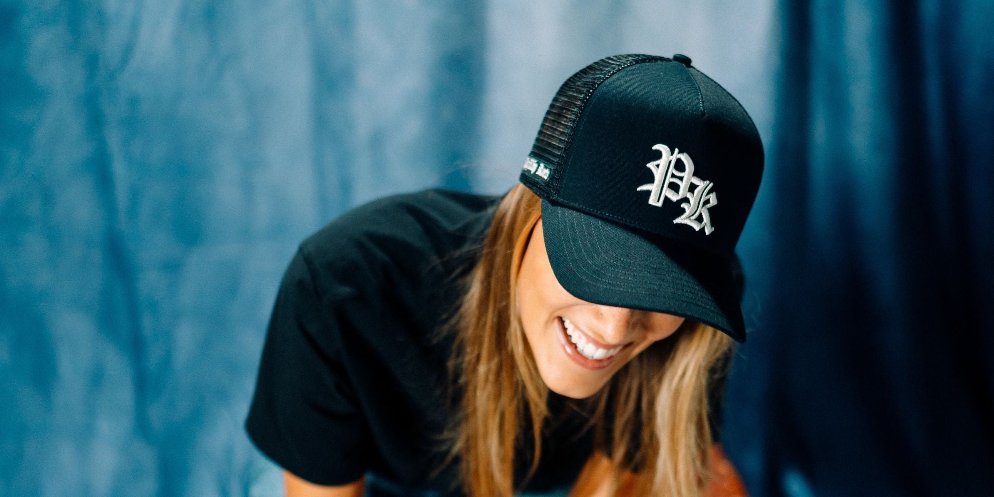 Person wearing a black PK cap with a PK logo against a blue curtain background