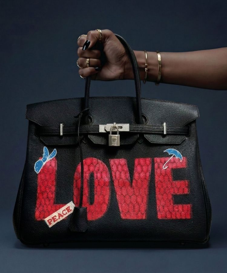 Black handbag with 'LOVE' and 'PEACE' text held by a hand against a dark background