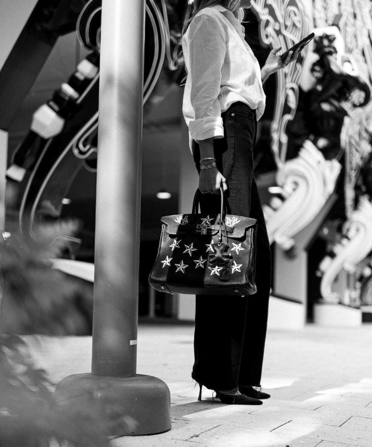 Person holding a large vintage Hermès handbag by Philip karto with star patterns on a city street.