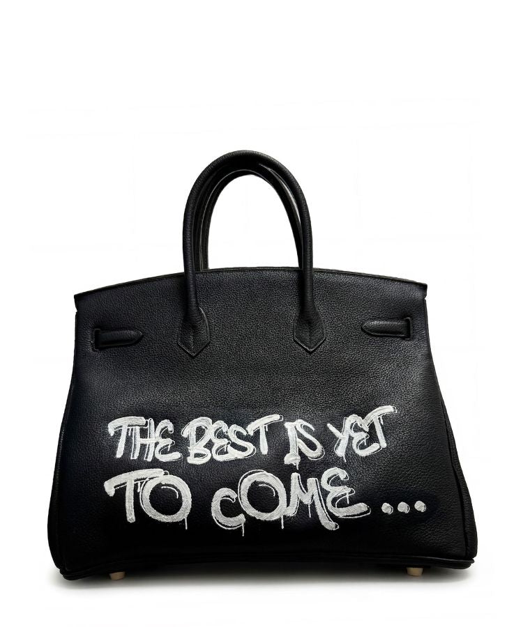 Philip Karto PK.02 The Best Is Yet To Come on bakc side of Birkin bag with white typographic script on black Hermès leather