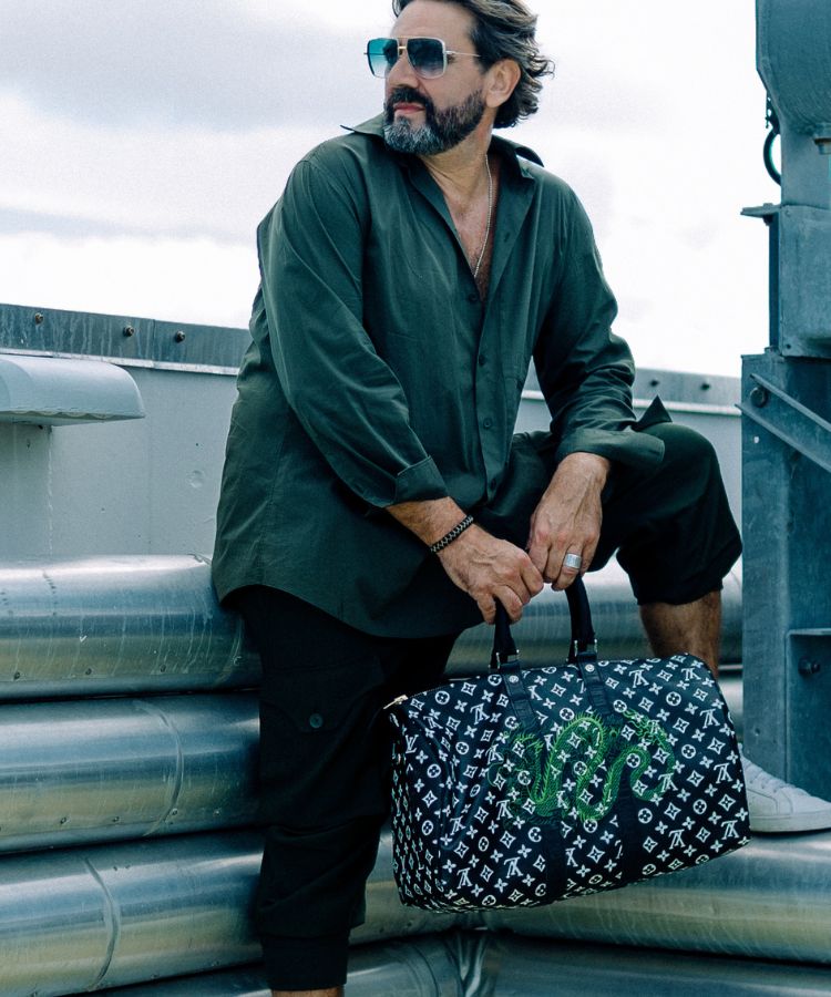 Man in green shirt and sunglasses holding a patterned Philip Karto handbag with Louis Vuitton monogram and green snake design