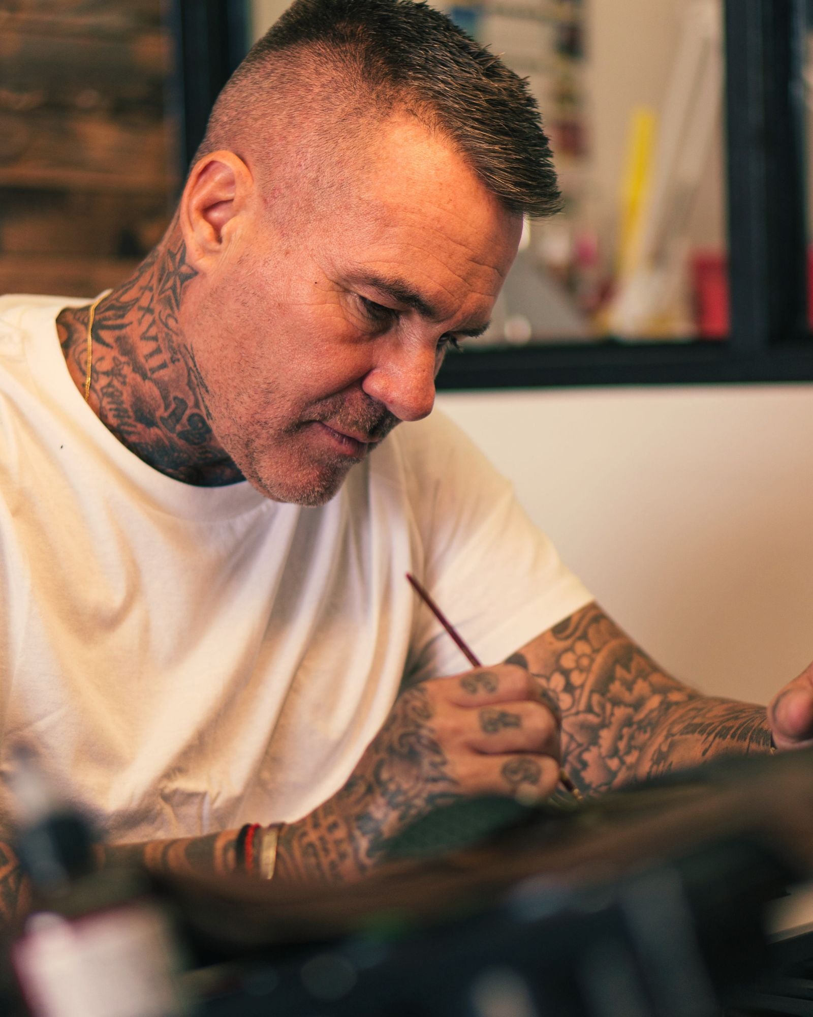 Philip Karto, with tattoos, working on a Louis Vuitton bag design, crasting a hand-painted artwork.