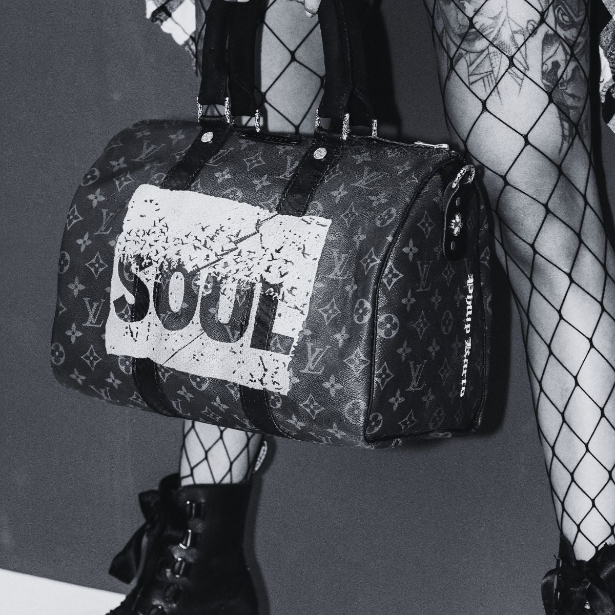 Louis Vuitton Keepall bag restored and transformed by philip Karto with SOUDL dign on it held by a preson with tattoos on the legs