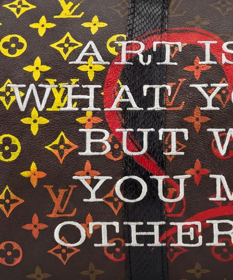 Close-up of a Louis Vuitton monogram canvas bag with bold white embroidered text reading 'ART IS WHAT YOU M OTHER' over a dark brown background with yellow, orange, and red monogram motifs.