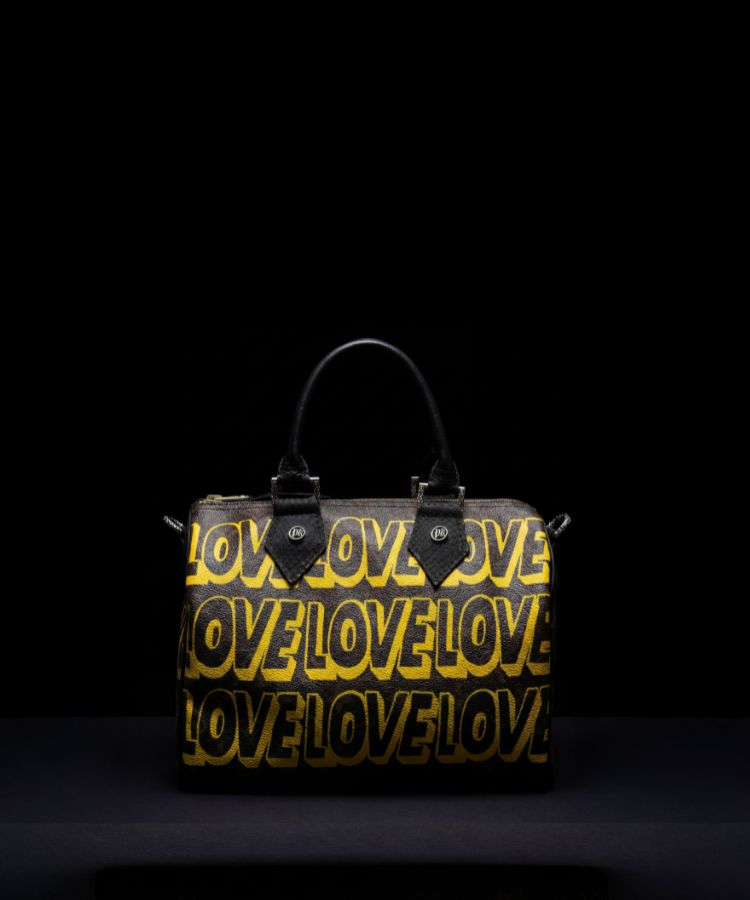 A black leather handbag with a repeating yellow 'LOVE' text pattern, featuring dual top handles and silver-tone hardware, set against a solid black background.