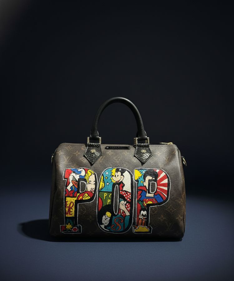 A dark brown monogram handbag with a black leather top handle, featuring large colorful 'POP' letter patches on the front with cartoon and anime-style illustrations, set against a dark studio background.