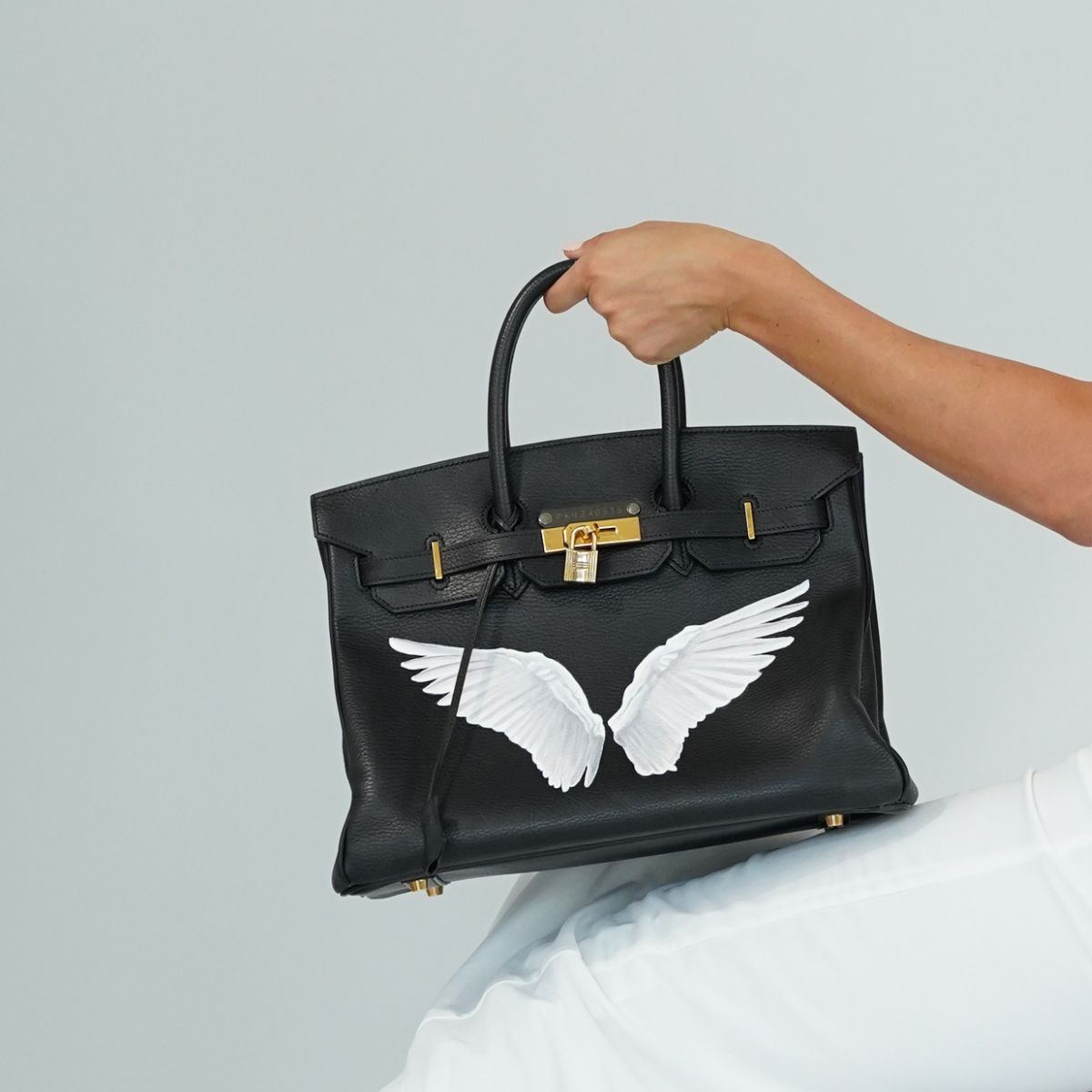 Hermès iconic Birkin bag in black, transformed by Philip Karto artwork, the collectible model is The Best I Yet To Come showning the front side of the Birkin with white hand-painted wings 