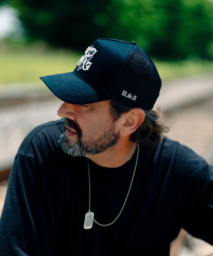 A man wearing a black trucker-style cap with a white embroidered logo and the text 'U.S.