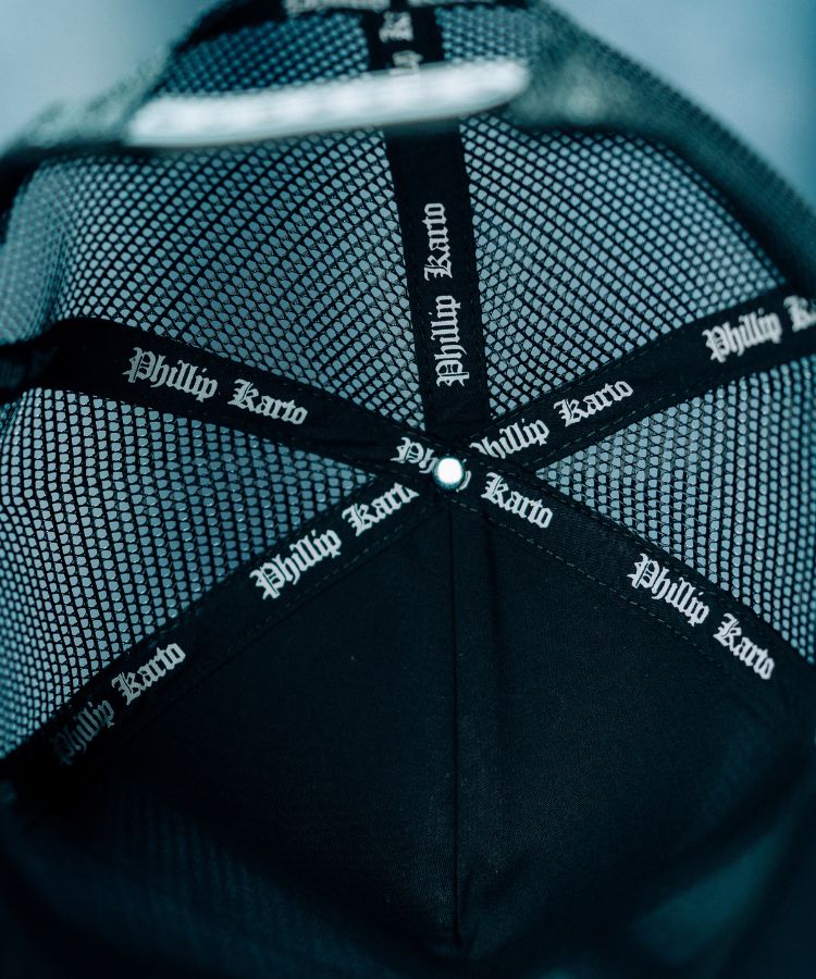 Inside of the Black PK cap with 'Phillip Karto' branding on the strap against a blurred background