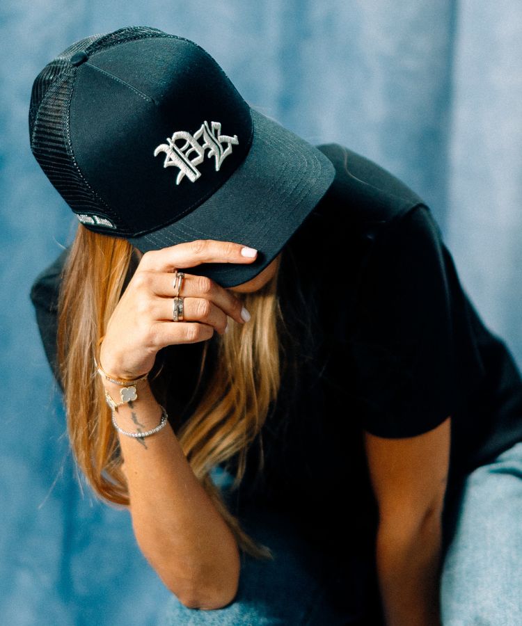 Person wearing the Black PK Cap with a PK logo by Philip Karto, sitting against a blue background