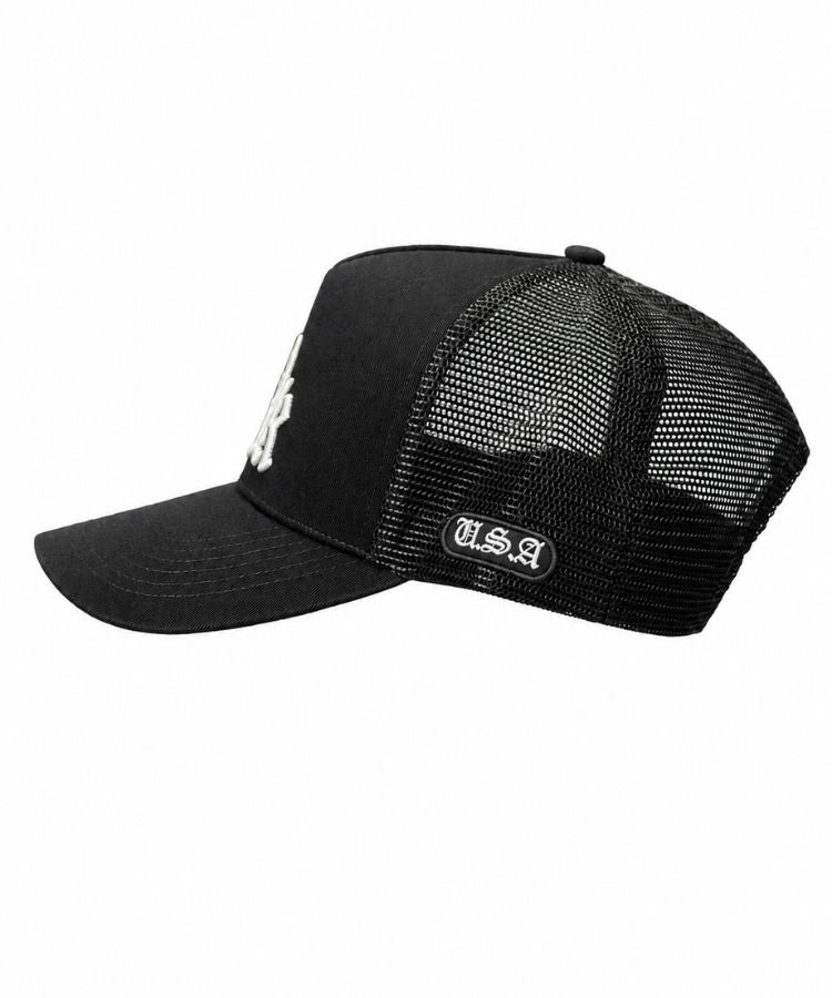 A black trucker-style baseball cap with a curved brim, black mesh back panels, a white embroidered 'PK' logo on the front, and a white 'U.S.A' on the side