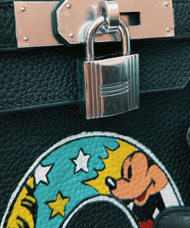 Close-up of a black leather bag with a silver padlock and a Mickey Mouse patch.