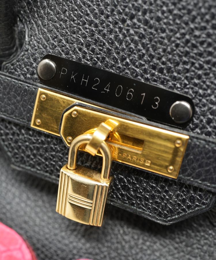 Close-up of a black leather handbag with a gold lock and visible brand name.