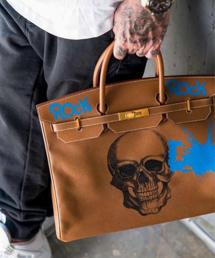 Brown vintage Hermès Birkin bag in leather with a skull design and 'ROCK' text, model ROCK'N ROLL by Philip Karto, held by a person.