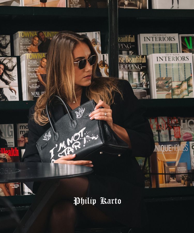 Woman holding a black vintage Hermès Birkin transformed by Philip Karto, model Stars, with text in a magazine-lined room