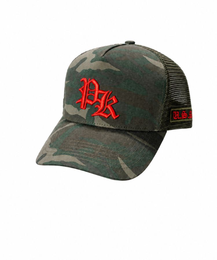 A camouflage trucker cap with a red embroidered 'PK' logo on the front and a red 'PK' patch on the side mesh by Philip Karto, shown on a plain white background.