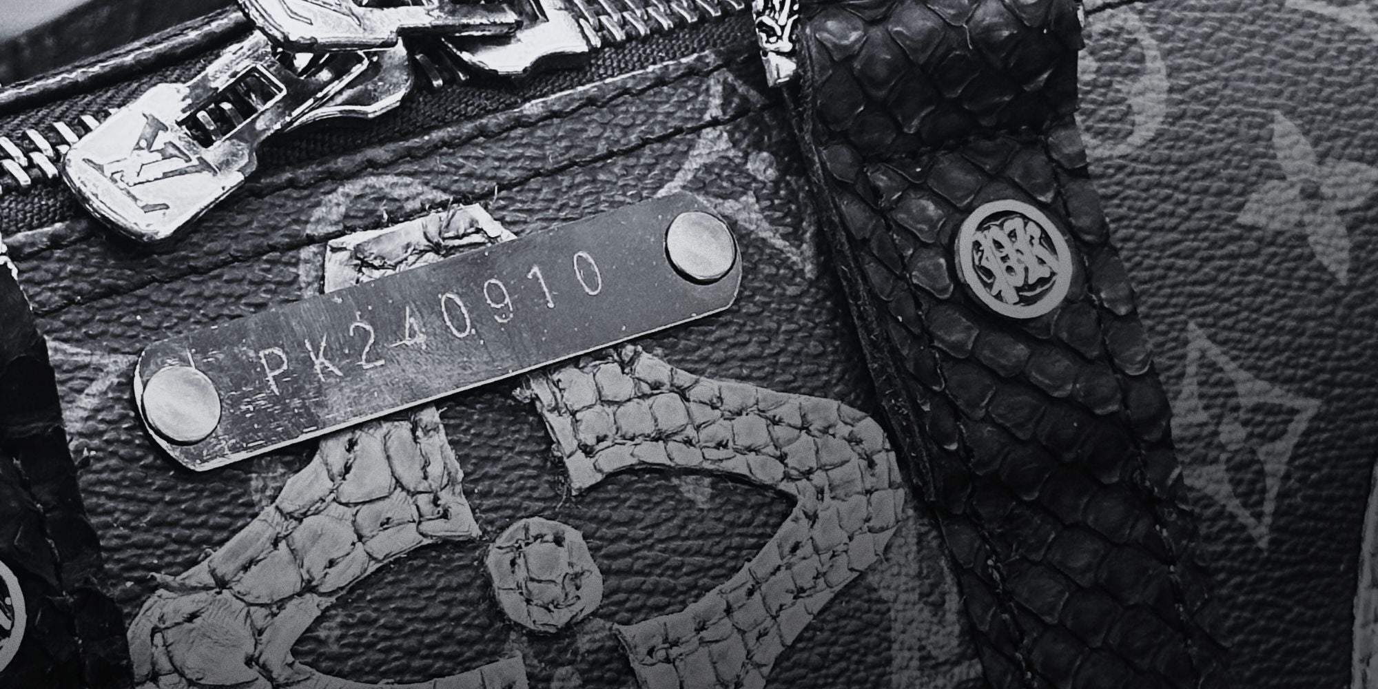 Details of a Philip Karto bag with the numeroted metal label on it in black and white. We can see the python skin details of the stripes, PK grommets and double zipper, plus the monogram patches.