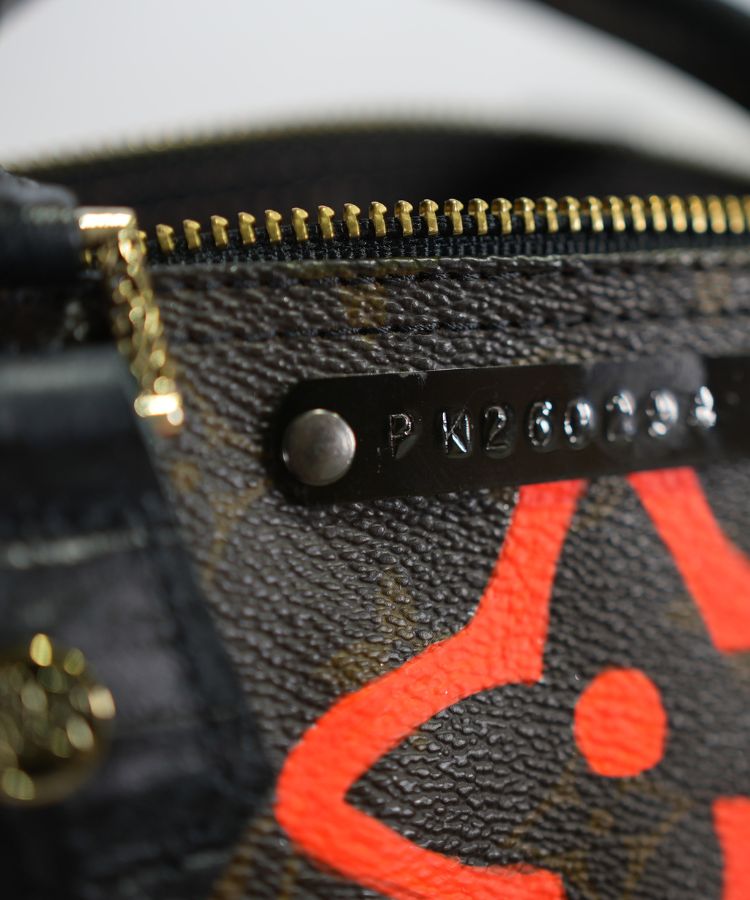Close-up of a LV monogram surface with a gold zipper and a black numbered plate on it, by Philip Karto