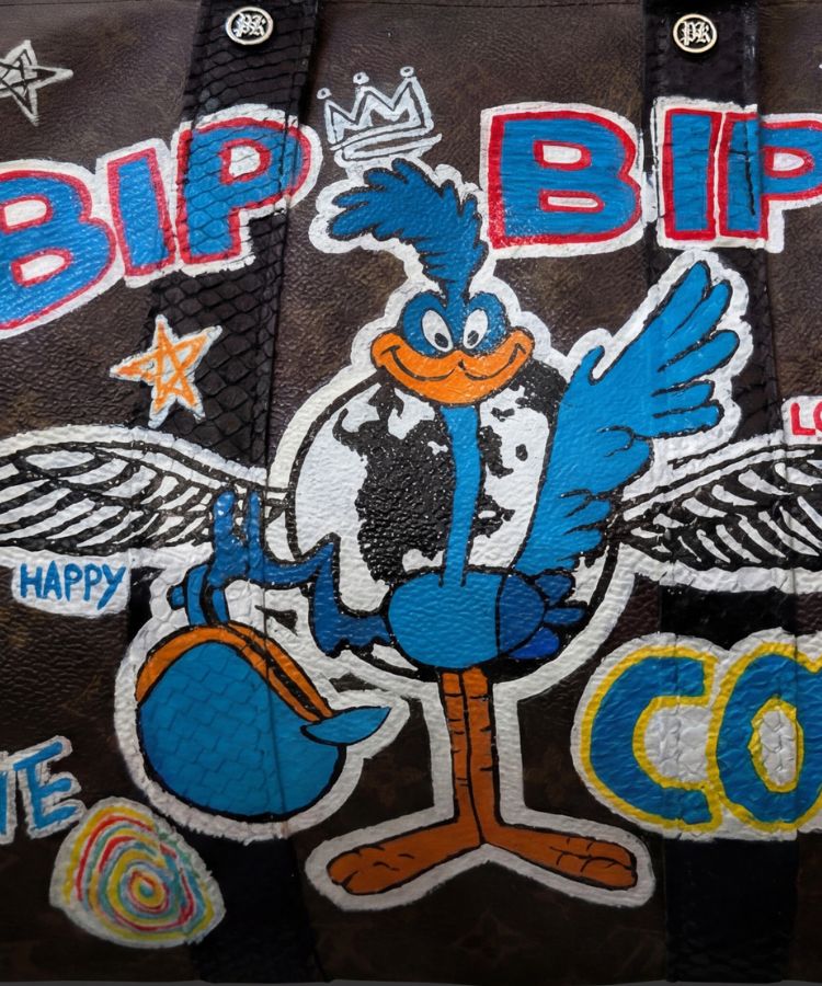 A close-up of a dark brown textured bag featuring a large embroidered patch of the cartoon character Road Runner, with colorful text and star motifs.