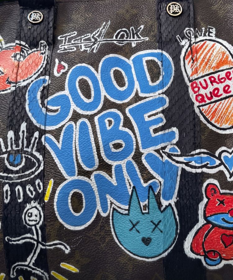 Close-up of a dark brown textured tote bag featuring colorful graffiti-style artwork and the text 'GOOD VIBE ONLY' in blue and white lettering.