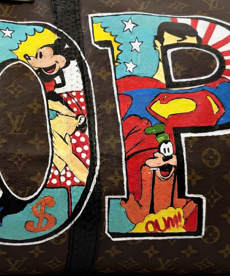 Close-up of a brown monogram bag with large decorative letters painted in a colorful pop-art style, featuring cartoon characters and stars.